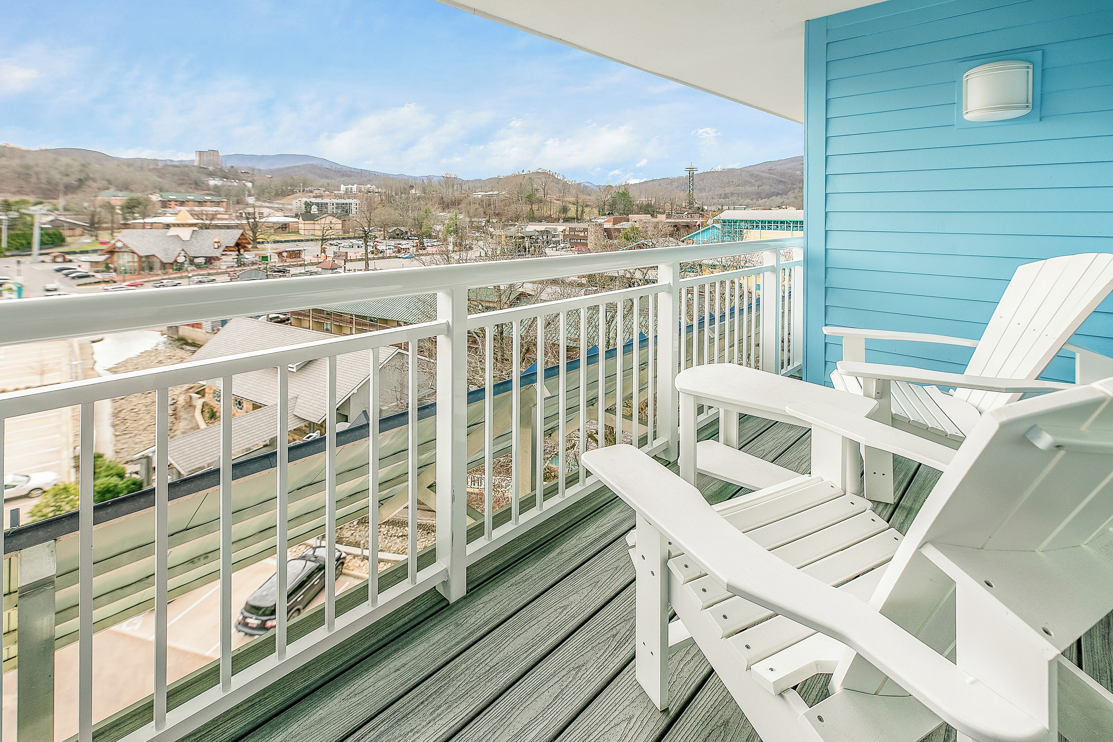 Ein Balkon mit weißen Stühlen, einer blauen Wand und Blick auf eine Stadt und Berge.