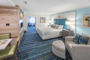 A hotel room with a large bed, a seating area with a table and chairs, a TV, and a view of the hallway.