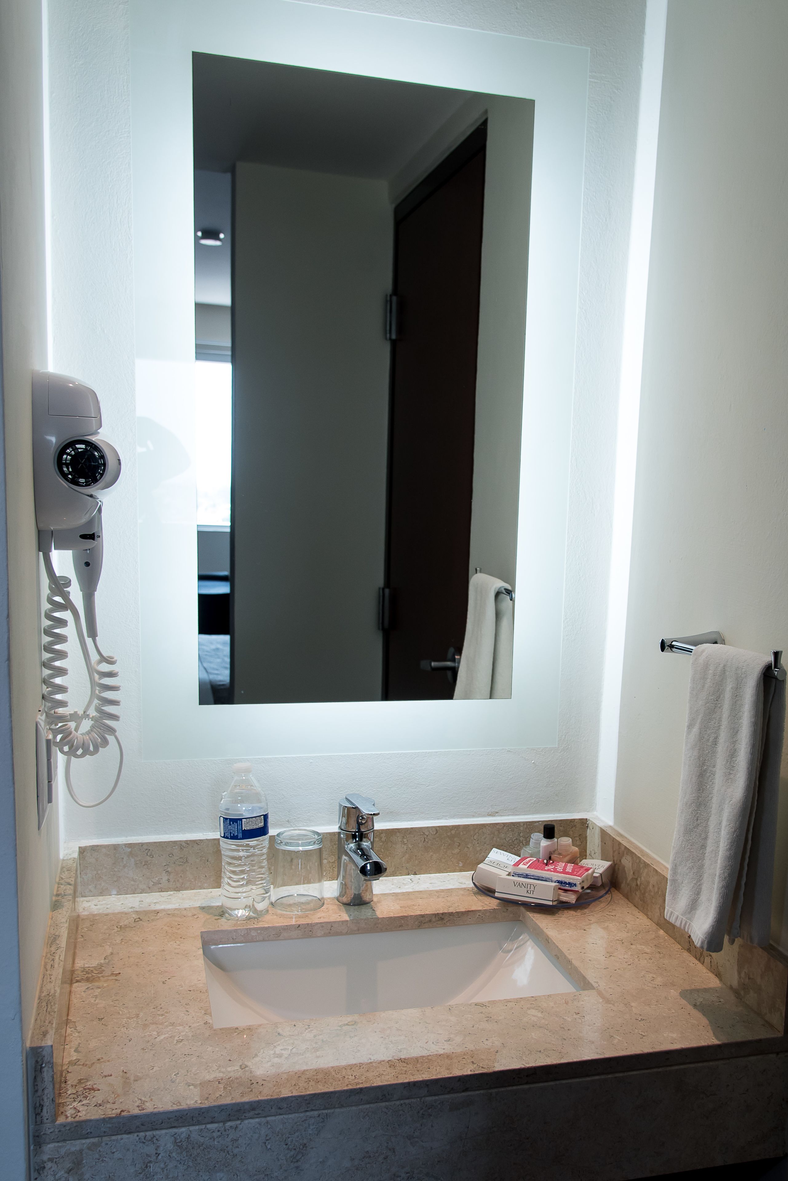 A bathroom with a sink, a mirror, a hairdryer, a towel, and a bottle of water.