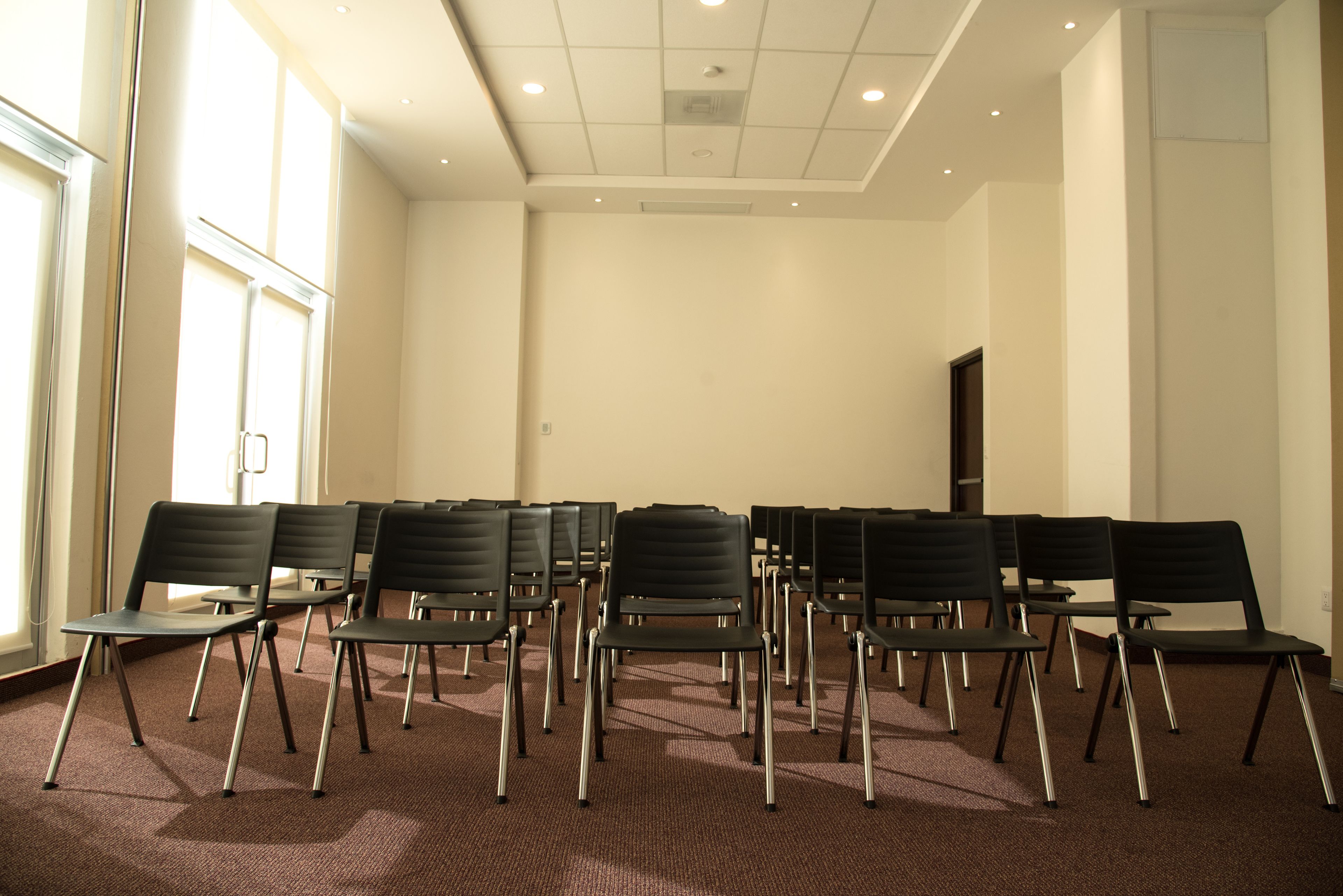Un salón de conferencias con filas de sillas negras y piso alfombrado.