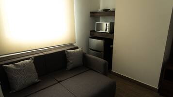 Un espacio habitable compacto con un sofá, dos almohadas, un microondas y un refrigerador.