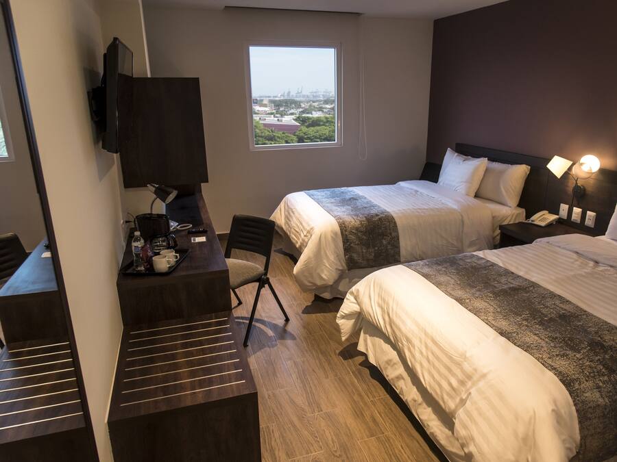 Une chambre d’hôtel avec deux lits, un bureau avec une chaise, un téléviseur fixé au mur et une fenêtre donnant sur la ville.