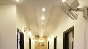 A hotel hallway with a polished floor, wall-mounted lights, and a ceiling fan. - Hotel New SS Residency (Amritsar)