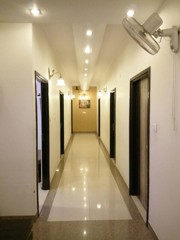 A hotel hallway with a polished floor, wall-mounted lights, and a ceiling fan. - Hotel New SS Residency (Amritsar)