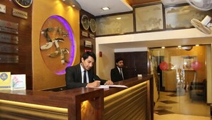 A reception desk with two staff members, a clock, and a wall with various signs. - Hotel New SS Residency (Amritsar)