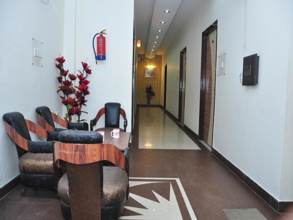 A hotel lobby with a reception desk, several chairs, a vase with red flowers, a fire extinguisher, and a hallway leading to rooms. - Hotel New SS Residency (Amritsar)