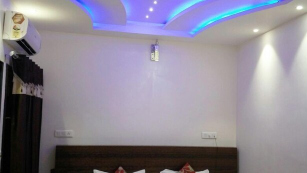 A bedroom with a modern ceiling design, a bed with floral pillows, and a bedside table with a lamp. - Hotel New SS Residency (Amritsar)