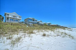 A beachfront property with multiple houses, including a large house with a balcony and a smaller house with a red roof.
