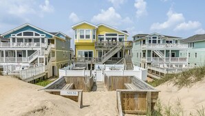 A beachfront property with multiple colorful houses, each with a balcony and a staircase leading to the beach. - Pebble Beach | Oceanfront | Dog Friendly, Private Pool, Hot Tub | Nags Head (Nags Head)