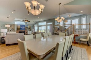 A spacious dining area with a large table and chairs, a ceiling fan, and a staircase leading to an upper level.