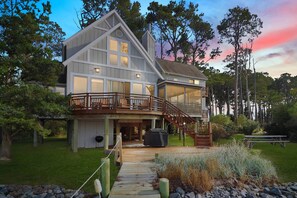 A large, modern house with a covered deck and a staircase leading to a second floor. - Grandview | Luxury Waterfront Sunset Views w/ Long Pier & Dock, Screened Porch, Kayaks + Pets (Chincoteague Island)