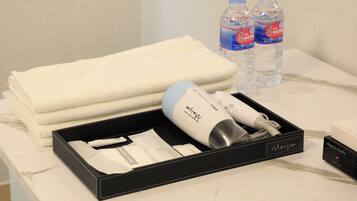 A hotel room with a neatly folded white towel, a hairdryer, a box labeled "Maison," and two bottles of water.