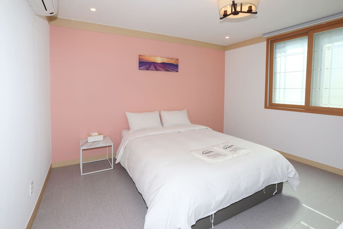A bedroom with a bed, a nightstand, a window, and a painting on the wall.
