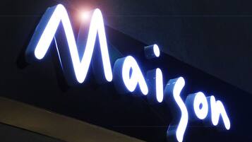 A neon sign with the word "Maison" in a cursive font.