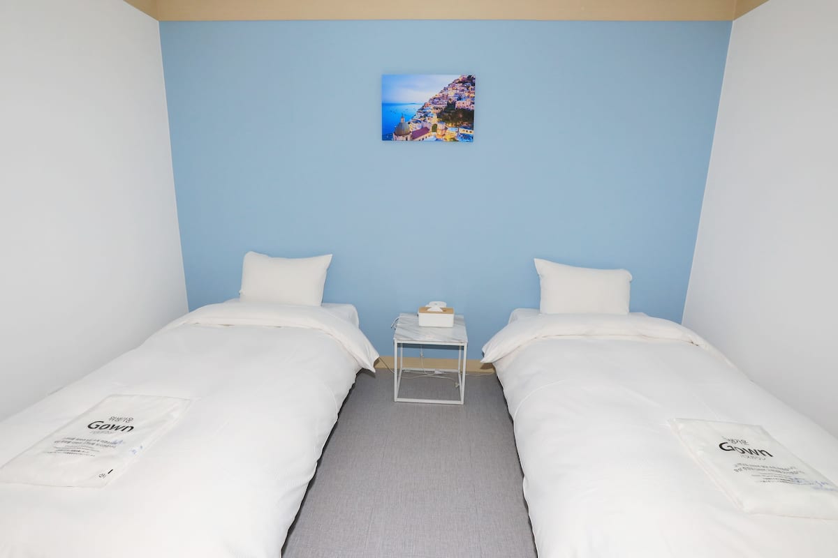 A room with two beds, a small bedside table with a tissue box, and a picture on the wall.