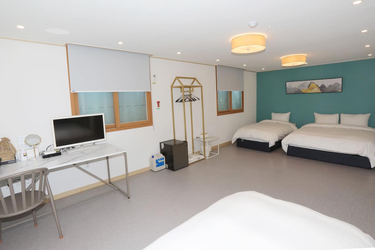 A hotel room with a desk, two beds, a TV, and a window.