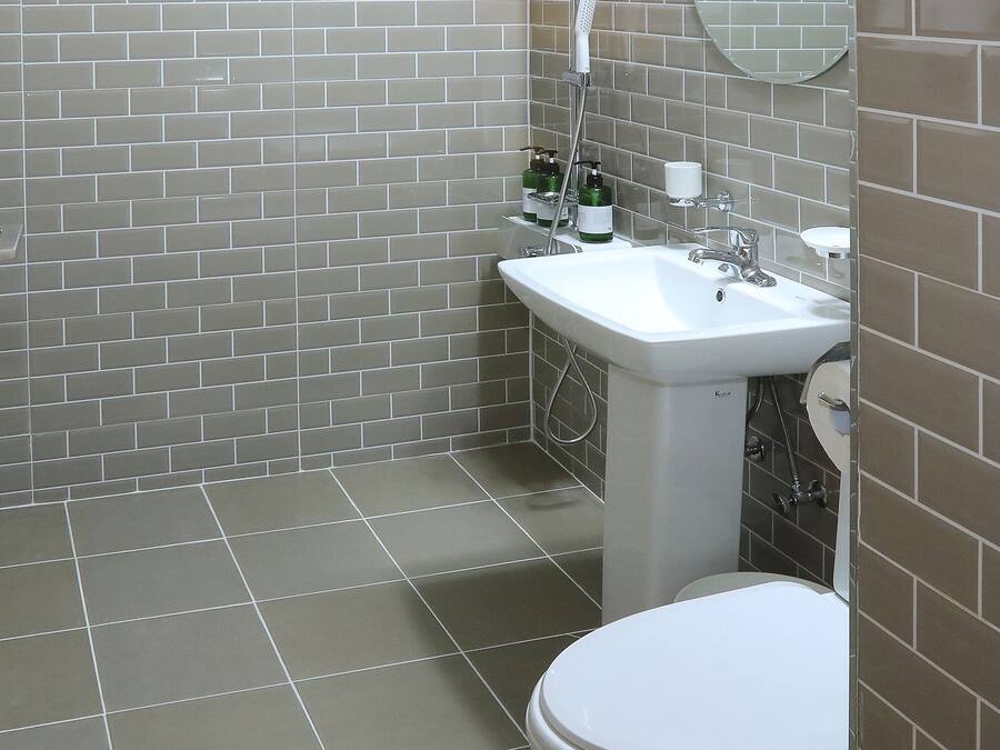 A bathroom with grey tiled walls, a white sink, and a toilet.