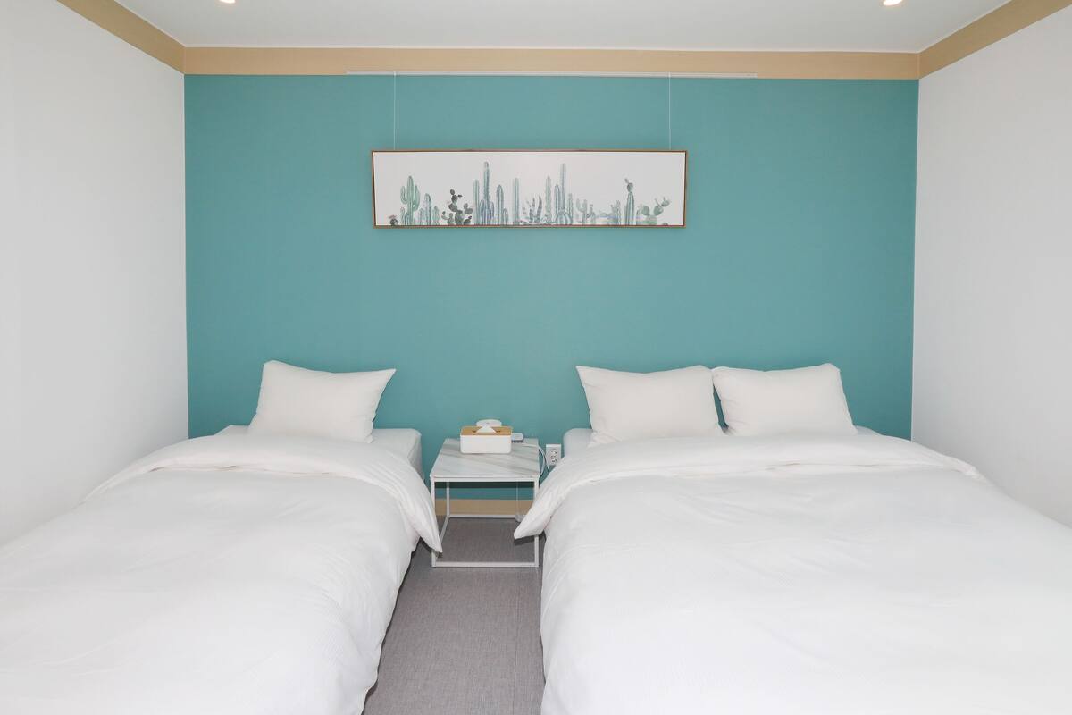 A hotel room with two beds, a teal accent wall, and a framed artwork above the beds.