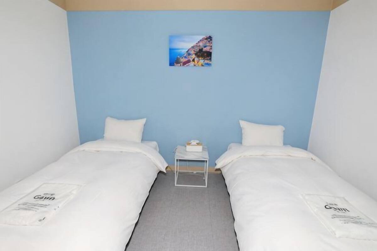 A room with two beds, a small table, and a picture on the wall.