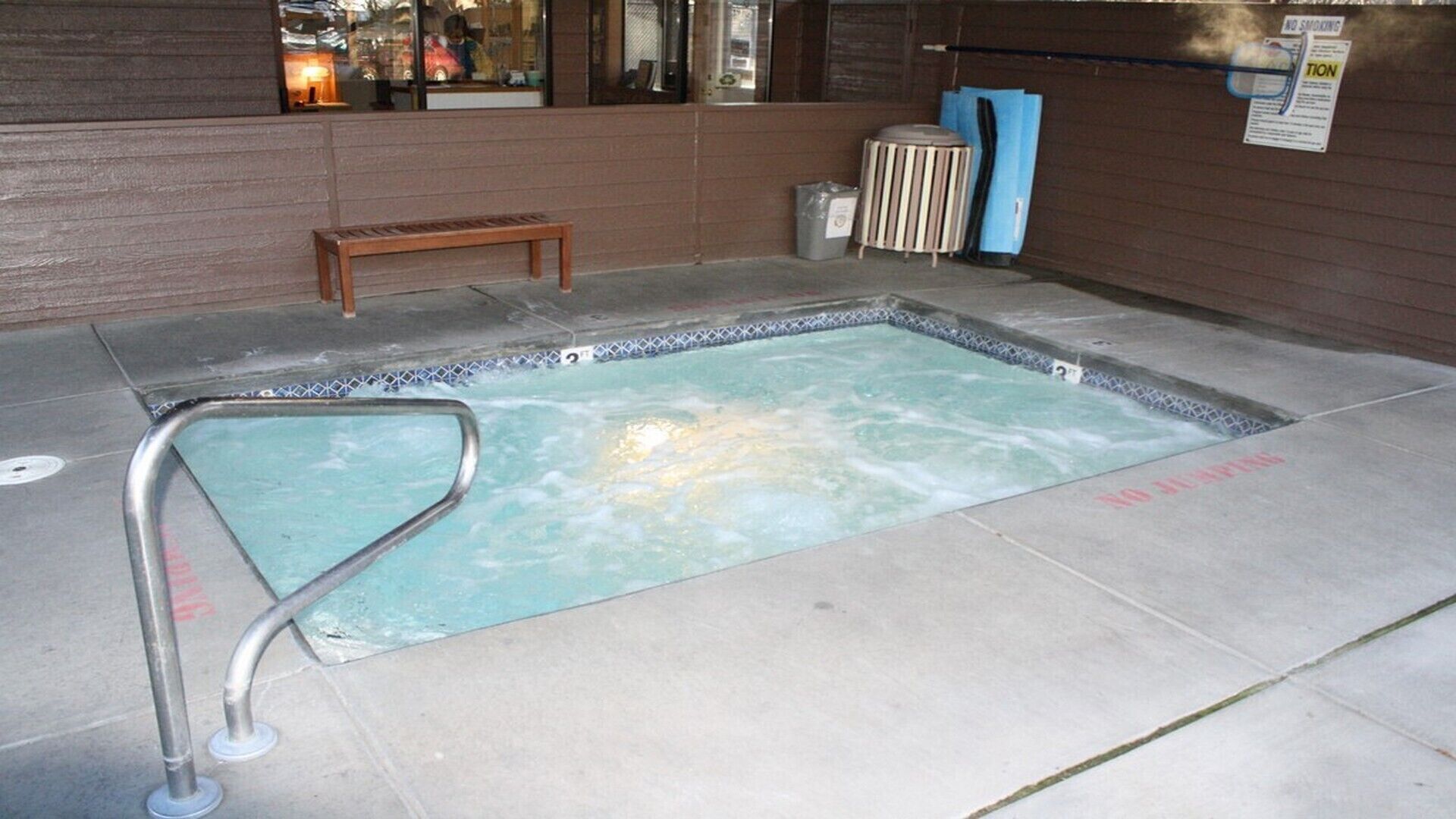 Un petit jacuzzi intérieur doté d’une rambarde de sécurité en métal, d’un banc en bois et d’une poubelle.