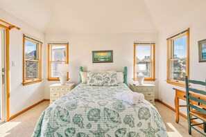 Una camera da letto con un letto, due comodini, una sedia e una finestra con un quadro.
