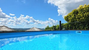 A clear blue swimming pool with a view of mountains and a thatched-roof structure in the background. - Family-friendly house in Draguć, Istria, with gorgeous garden and stunning view (Cerovlje)