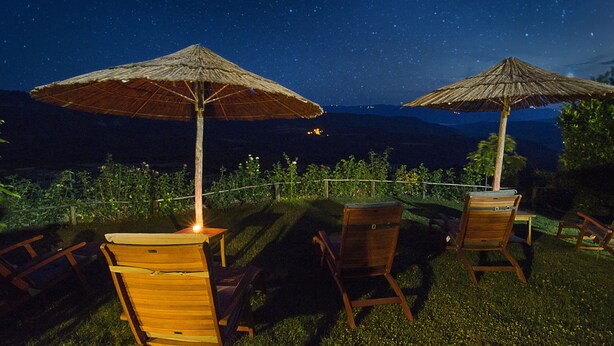 Two wooden chairs and two thatched umbrellas on a grassy lawn with a night sky view. - Family-friendly house in Draguć, Istria, with gorgeous garden and stunning view (Cerovlje)