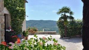 A view from a covered patio with a stone building, potted plants, and a palm tree. - Family-friendly house in Draguć, Istria, with gorgeous garden and stunning view (Cerovlje)