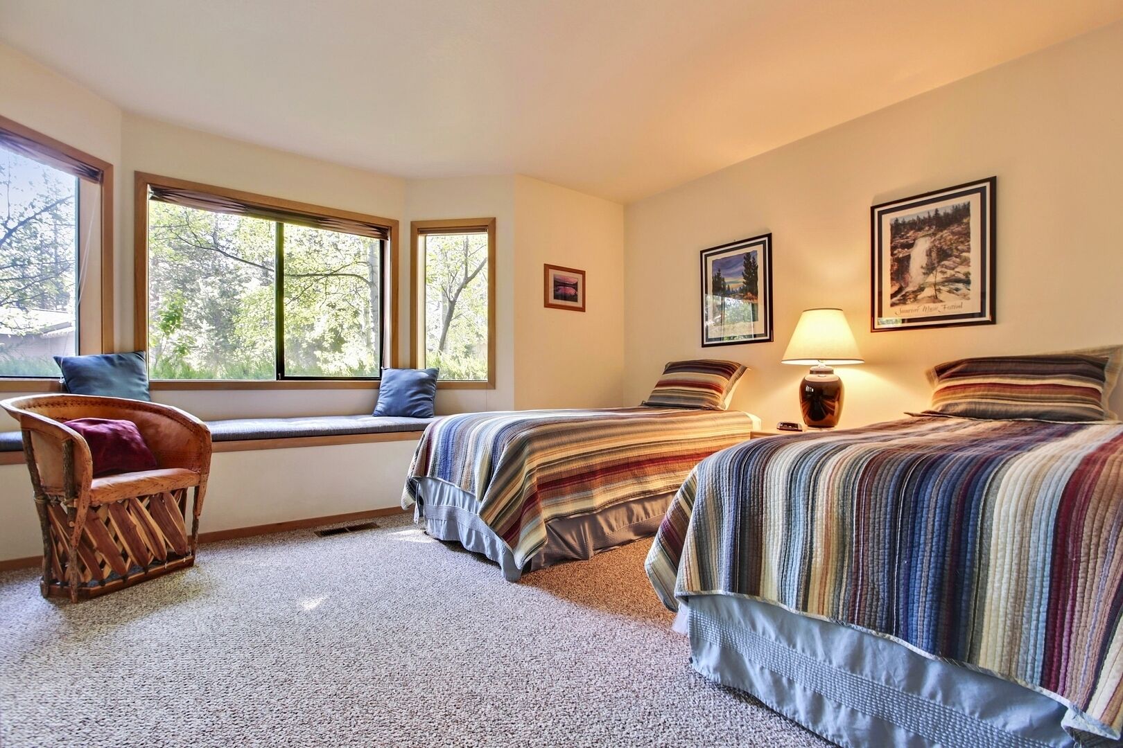 A bedroom with two beds, a window seat, a chair, and a lamp.