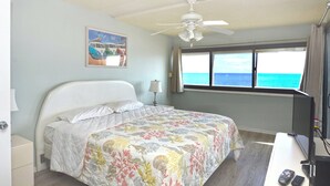 Ein Schlafzimmer mit Bett, Deckenventilator, Fenster mit Meerblick und Fernseher auf einem Schreibtisch.