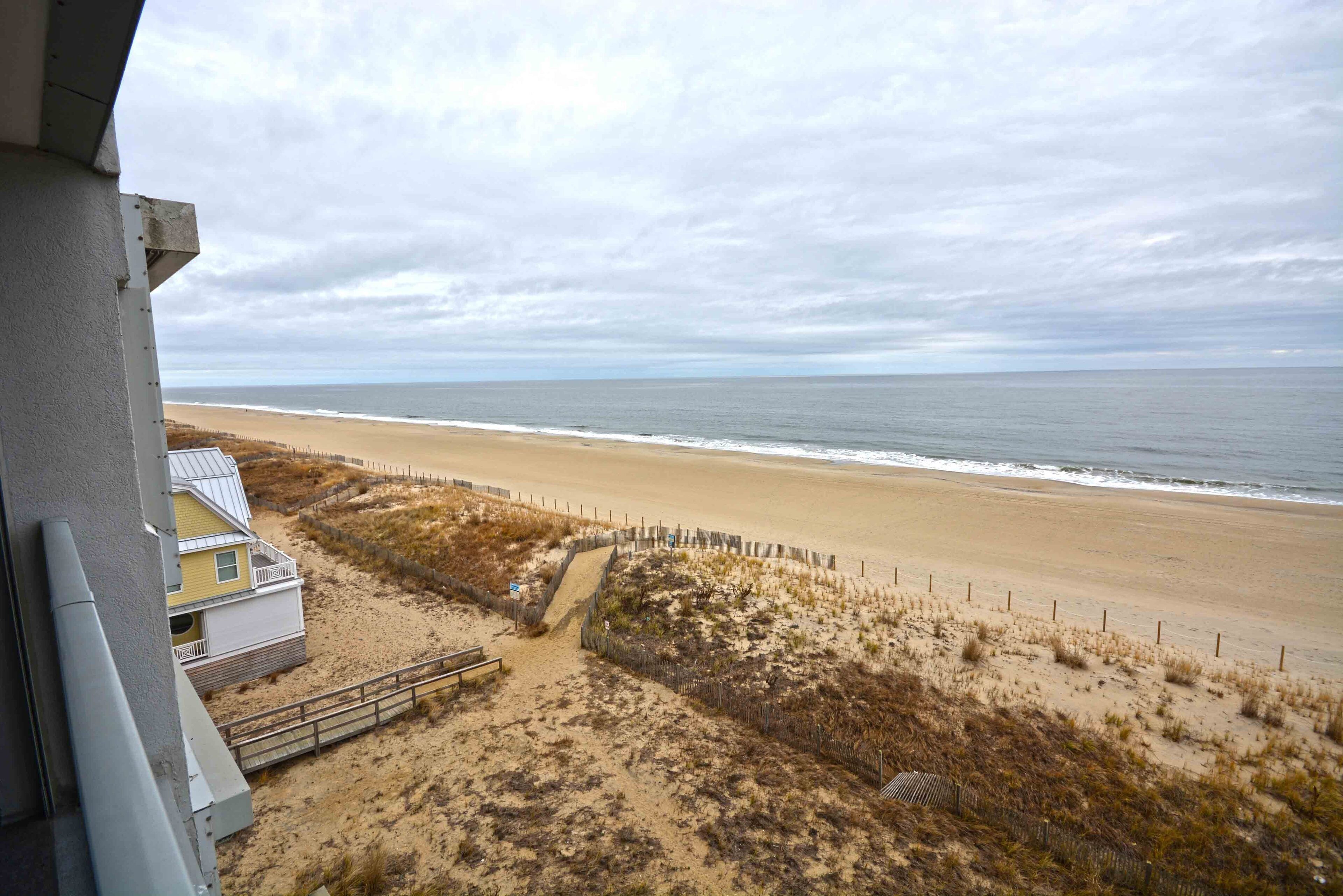 A beach view with a sandy path leading to a building with a balcony.