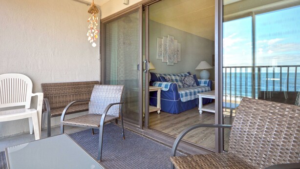 Ein Balkon mit Korbmöbeln, eine Glastür zu einem Raum mit einem blauen Sofa und Blick auf das Meer.