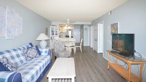 Ein Wohnzimmer mit einem blau-weißen karierten Sofa, einem weißen Couchtisch und einem Fernseher auf einem Holzständer.