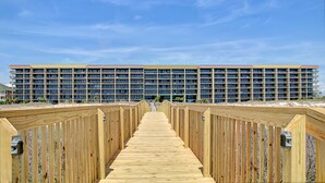 Un paseo marítimo de madera que conduce a un edificio grande de varios pisos, con numerosas ventanas y balcones.