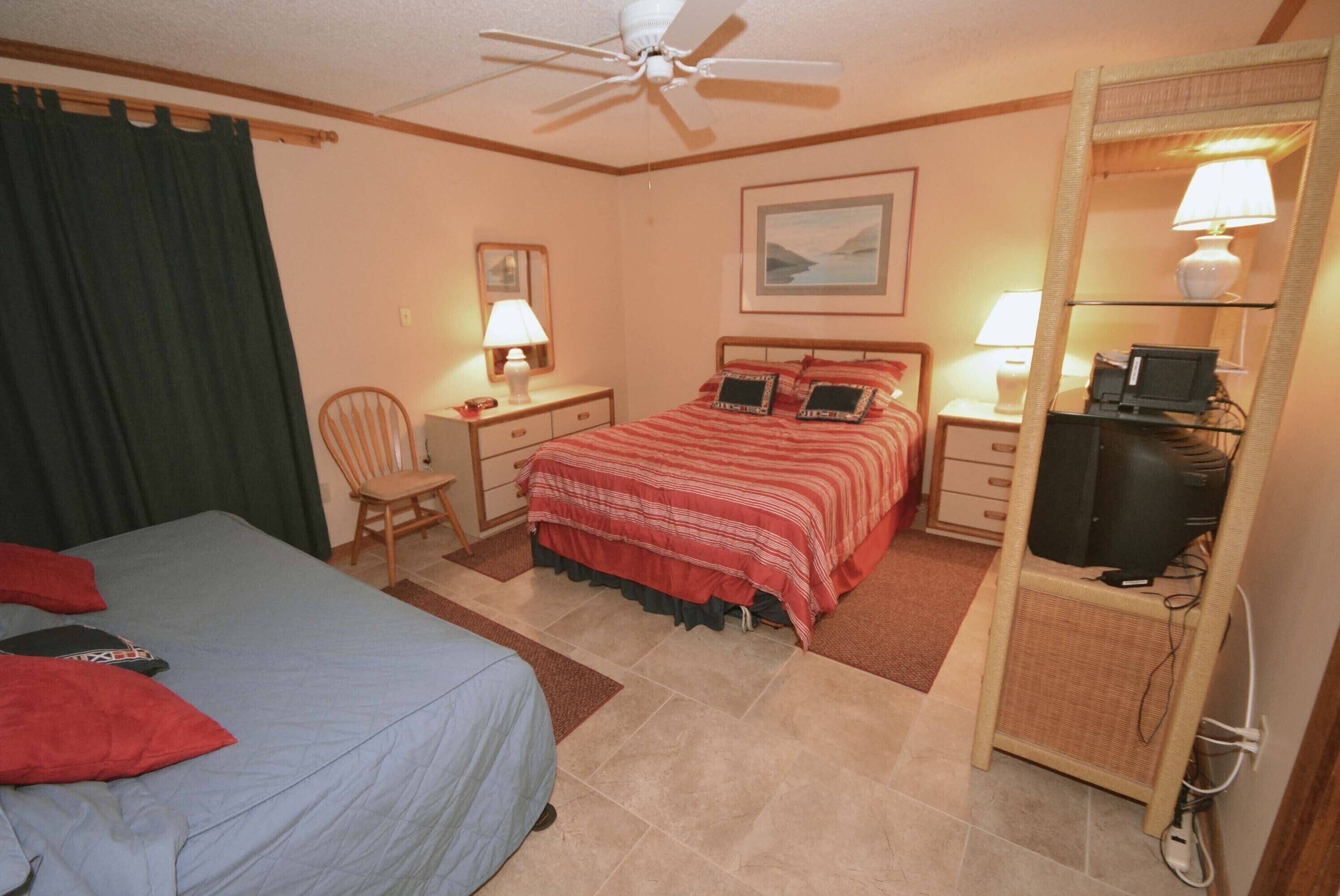 Une chambre d’hôtel équipée d’un lit, d’un bureau avec un ordinateur, d’une chaise et d’un ventilateur de plafond.