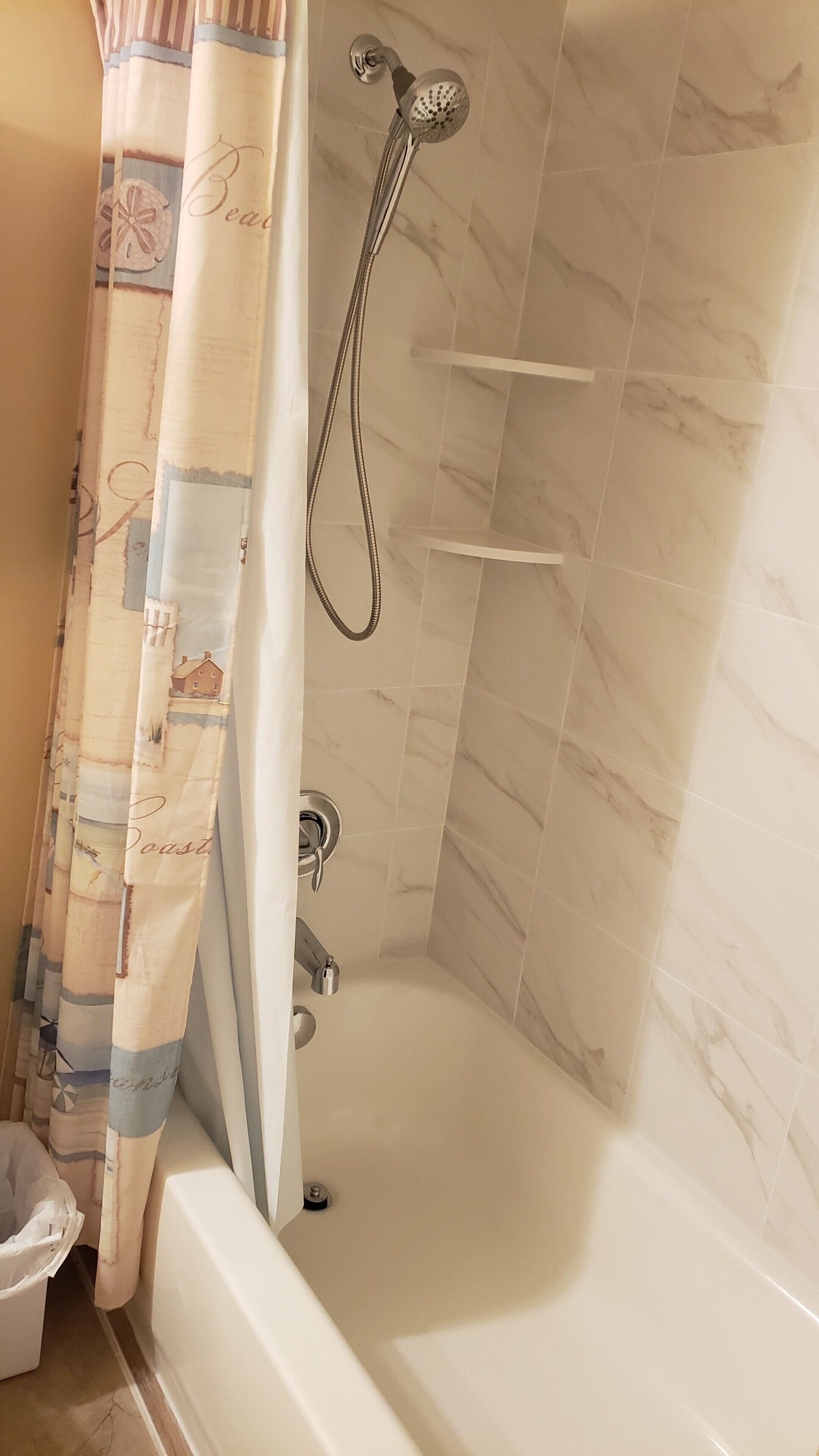 Un baño con bañera, ducha y cortina decorada con motivos playeros.