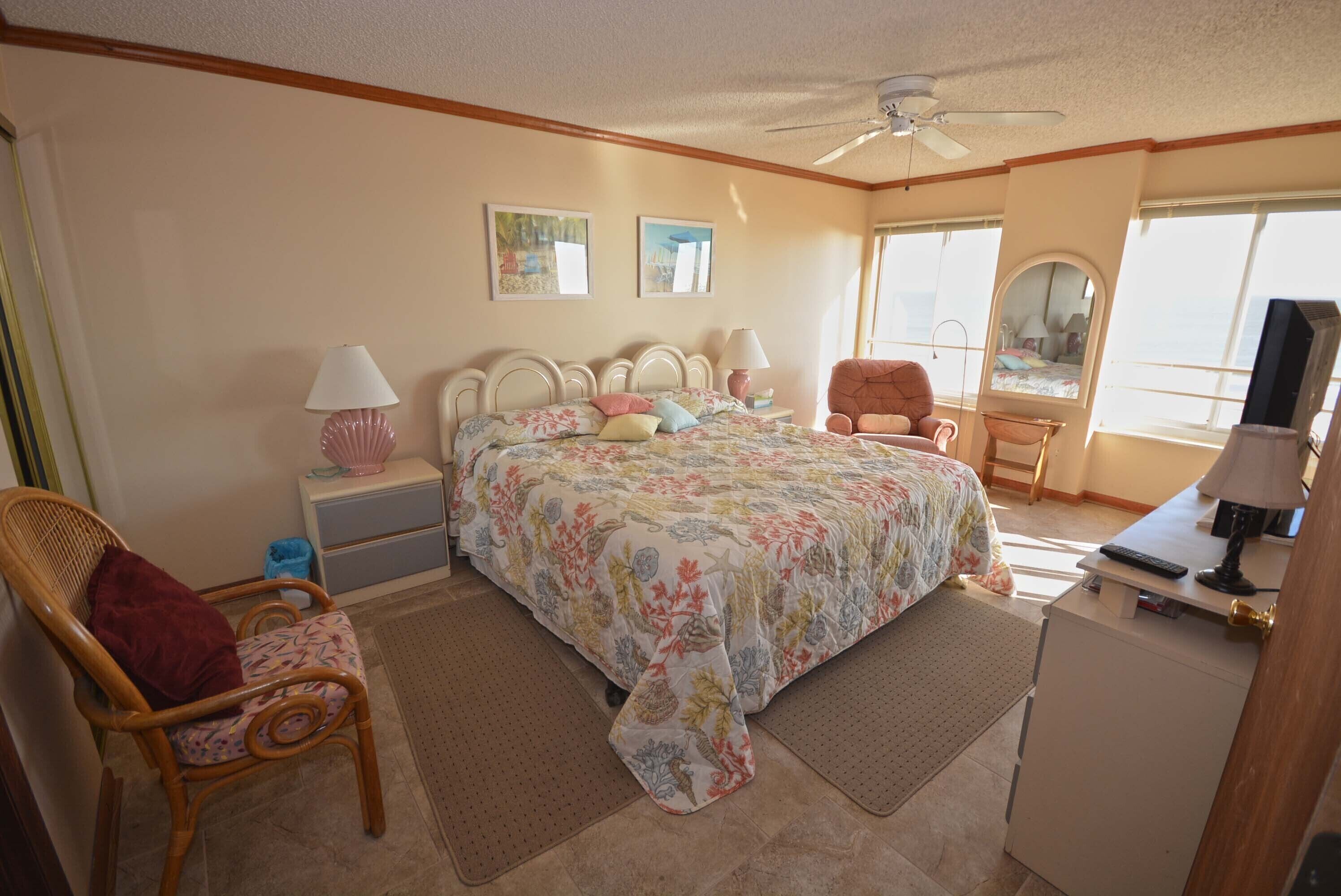A bedroom with a bed, a chair, a desk, a mirror, and a ceiling fan.