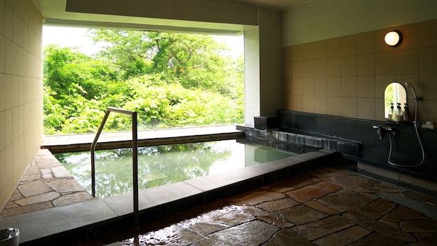 Un área de spa con suelo de piedra, una bañera de hidromasaje con cerramiento de cristal y vistas a la vegetación exuberante.