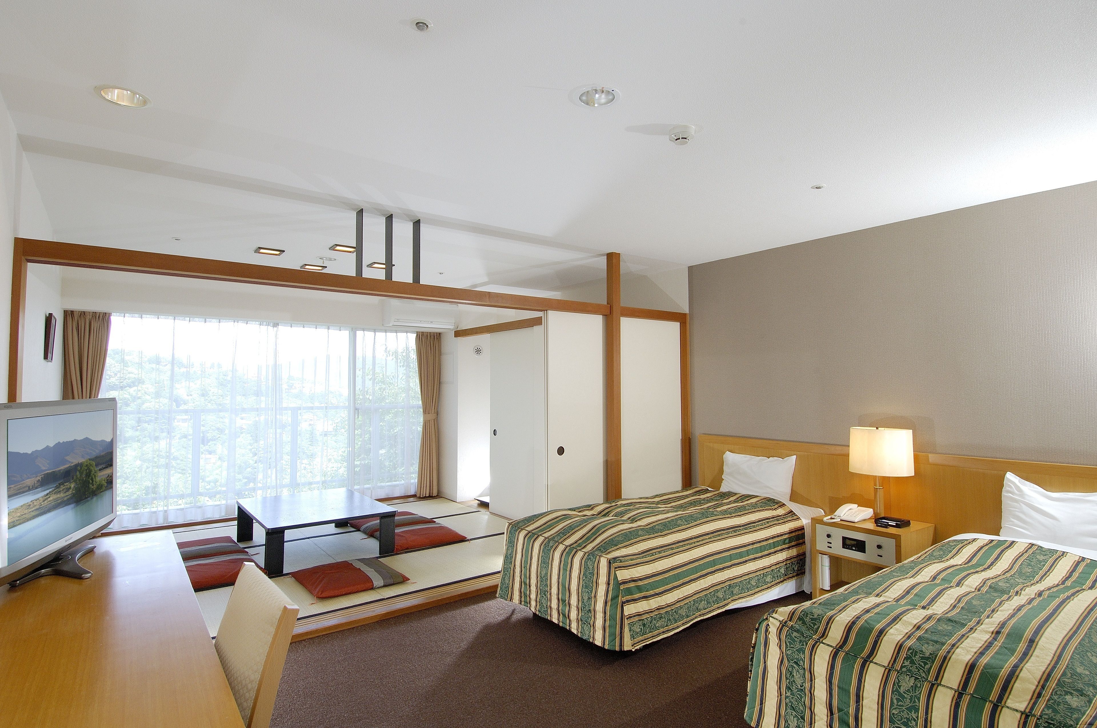 A hotel room with two beds, a desk, a TV, and a window with curtains.