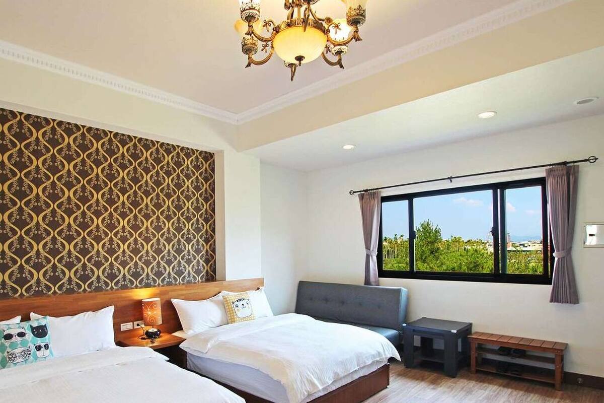 A hotel room with two beds, a chandelier, a large window with a view, and a patterned wallpaper.