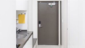A modern, white-walled kitchen with a washing machine, a sink, and a door with a lock.