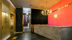Ein Hotel-Rezeptionsbereich mit Marmor-Theke, einer roten Wand mit dem Hotelnamen und einer Kristallleuchtre.