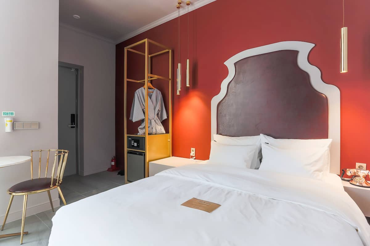 Una habitación de hotel con una cama, una silla, un armario y un escritorio con una lámpara.