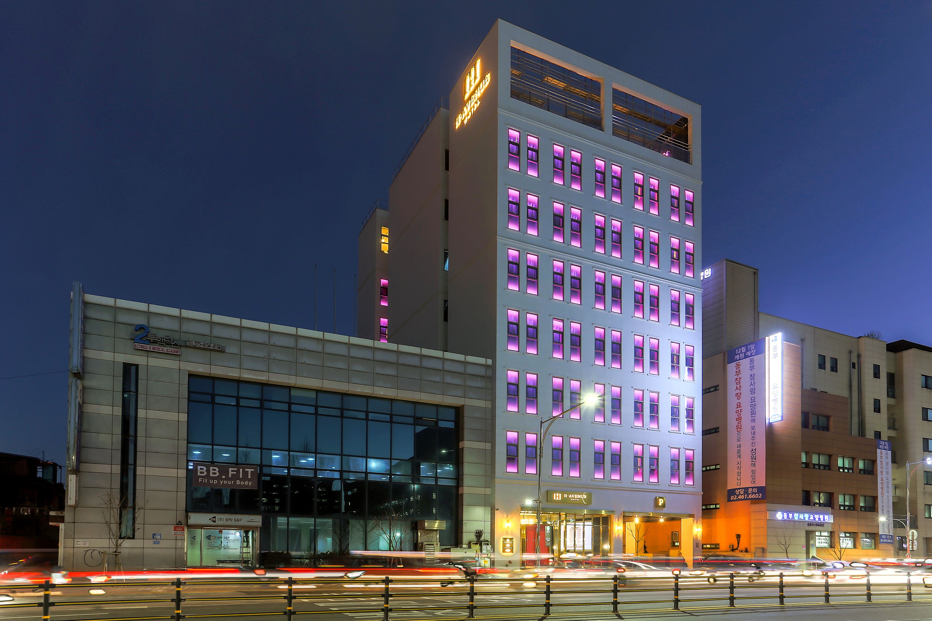 A modern hotel with multiple floors, large windows, and illuminated signage.