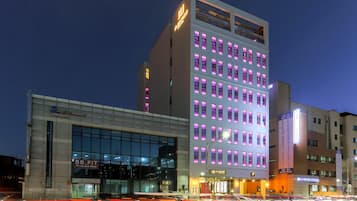 A modern hotel with multiple floors, large windows, and illuminated signage.
