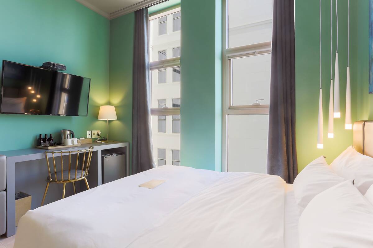 Habitación de hotel con cama, escritorio, televisor y ventana con cortinas.