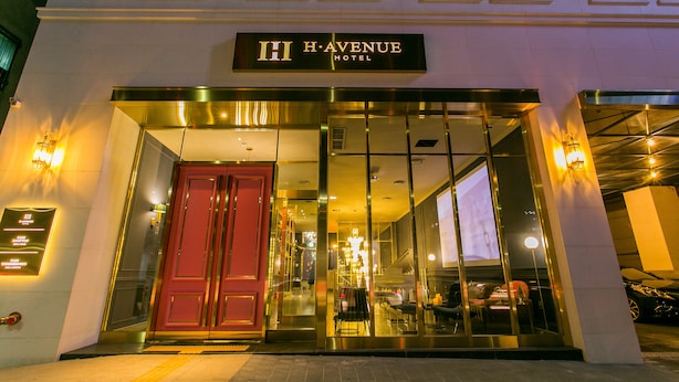 Das HI HAVENUE HOTEL mit einem markanten Eingangsbereich, beleuchteter Beschilderung und einem modernen architektonischen Design.