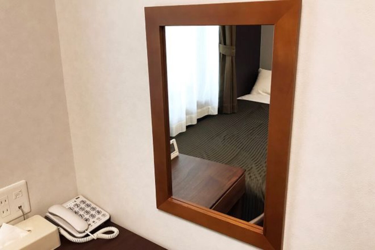 A hotel room with a wooden-framed mirror reflecting a bed, a bedside table, and a telephone.