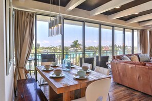 A dining area with a wooden table set for four, a leather sofa, and a view of a pool and buildings. - Direct Beach Access, and Amazing Views. Beachfront Pool, Huge Balcony and Fabulously Appointed Condo (Treasure Island)