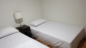 A simple, clean room with two single beds, a nightstand with a lamp, and a wooden floor. - Galaxy Gangnam 2 (Seoul)